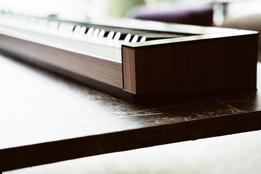 Modern digital piano with a sleek wood-grain finish resting on a dark marble-patterned table.