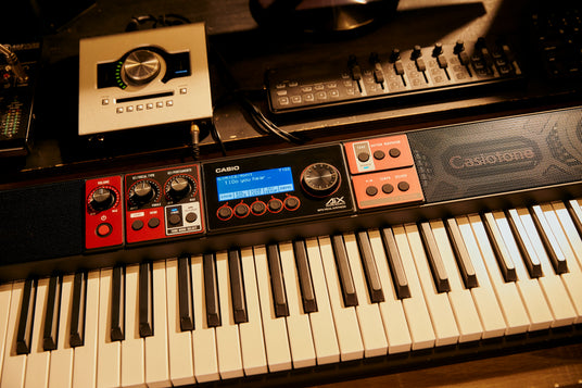 Casio CT-S1000V keyboard with red control panels, LCD screen, and black keys, positioned next to studio audio equipment.