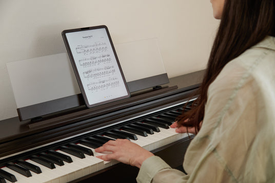 Person playing a dark wood digital piano with a tablet displaying Chopin sheet music on the stand.