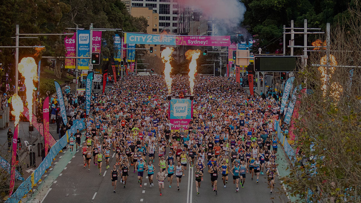 Massive crowd of runners starting the City2Surf race in Sydney with flames and colorful banners lining the street.