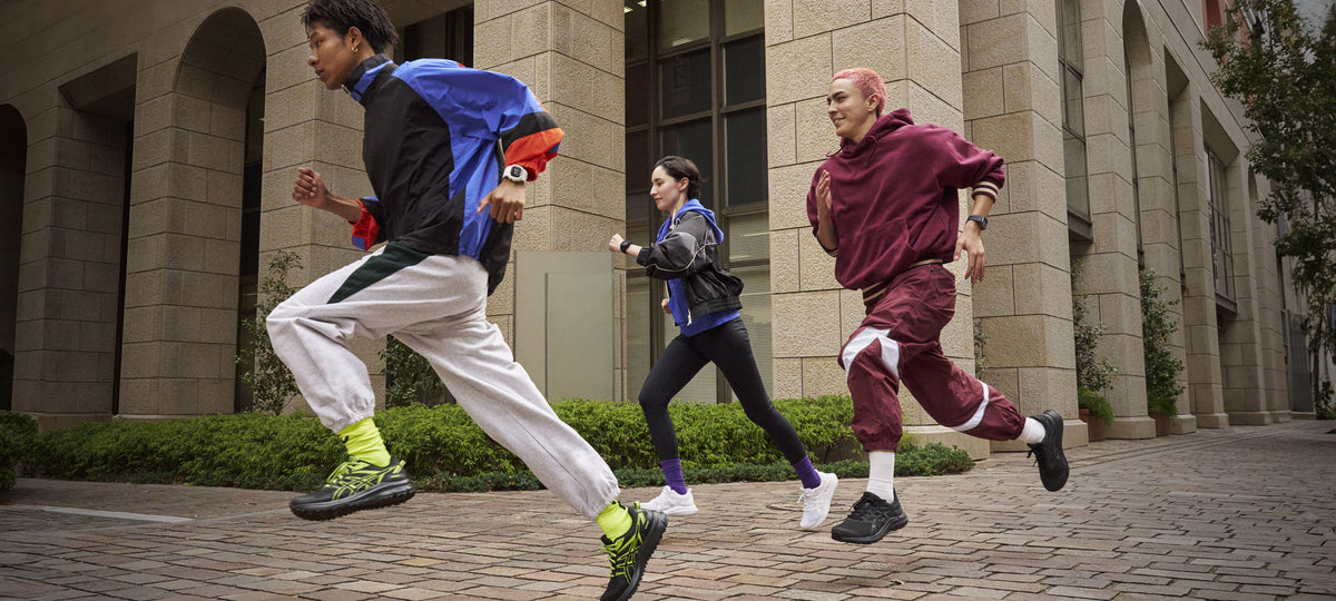 Three people in stylish sportswear running together on a cobblestone path in front of a modern stone building.