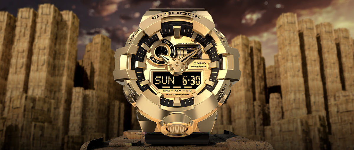Gold G-Shock GM700 watch with a metallic finish and digital-analog display against a rugged desert rock background.