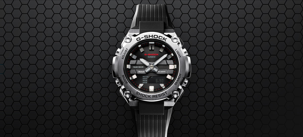 Silver and black G-Shock watch with a stainless steel bezel and textured black resin strap against a dark honeycomb background.
