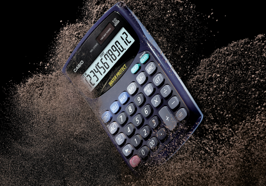 Casio WD-220MS dust-proof calculator surrounded by swirling dirt particles against a black background.