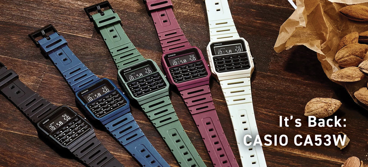 Four Casio CA53W calculator watches in black, blue, green, maroon, and white on a wooden surface with almonds.