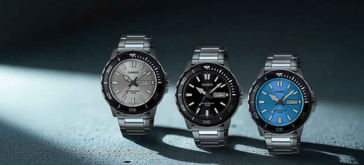 Three Casio MTD125D stainless steel watches with silver, black, and blue dials on a textured dark surface.
