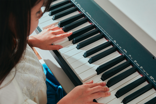Young girl playing a slim black Casio digital keyboard with white and black keys from an overhead perspective.