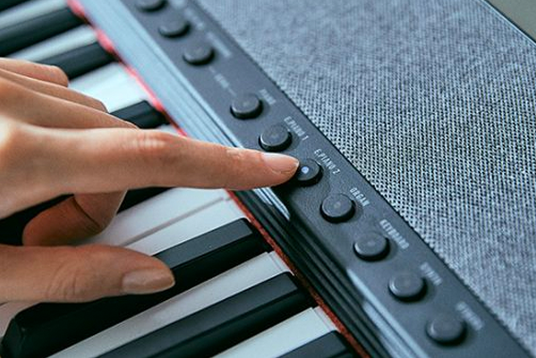 A hand pressing a button on a sleek black Casiotone CT-S1 keyboard with a textured grey fabric speaker grille.