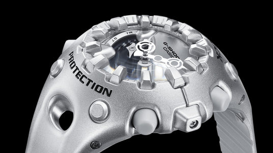 Close-up of a silver G-Shock watch with a rugged, metallic bezel and bold Protection lettering against a black background.