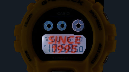 Bright yellow G-Shock digital watch face with a glowing backlight displaying the time and date against a dark background.
