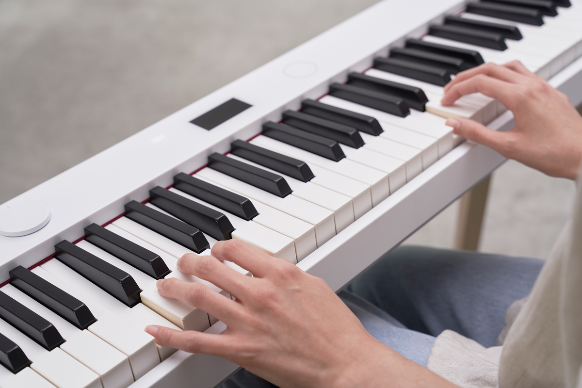 Hands playing a modern white digital piano with black and white keys in a bright, minimalist setting.