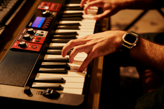 Hands playing a black and red Casio digital keyboard with a metallic wristwatch visible on the wrist.