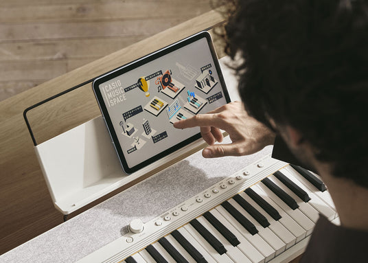 Person using a tablet app on a white Casio digital keyboard to navigate music learning features.