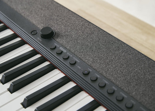 Modern digital piano with a fabric-covered speaker panel, black control buttons, and a volume knob above white keys.