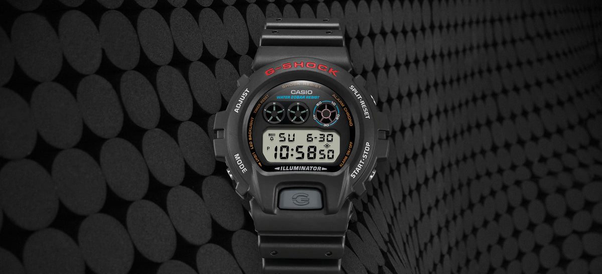 Black Casio G-Shock digital watch with red lettering and blue accents against a textured dark circular background.