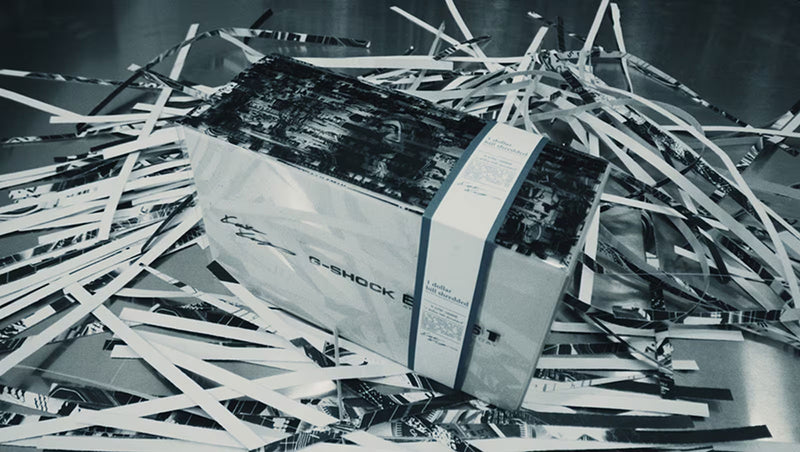 Casio G-Shock box by Kosuke Kawamura wrapped in a paper band, surrounded by shredded dollar bill collage strips.