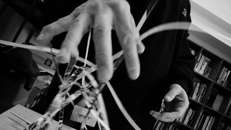 Close-up of hands manipulating shredded paper strips in a black and white artistic collage style.