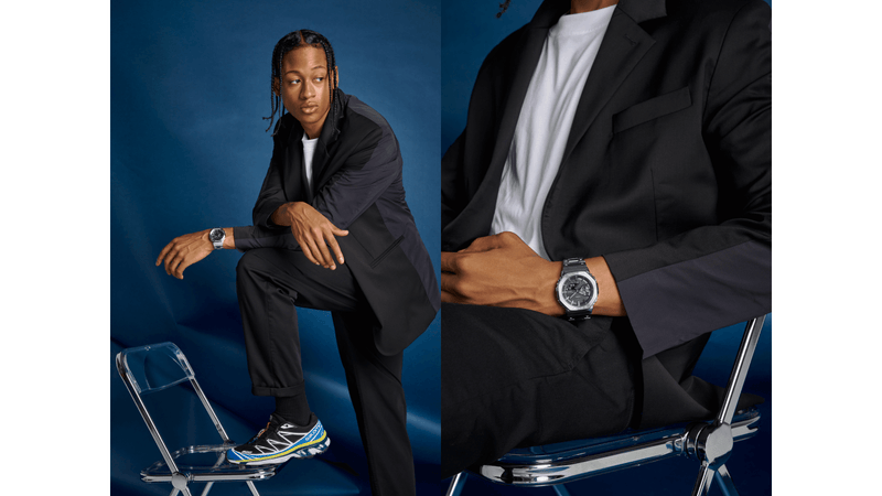 Man in a black suit wearing a silver Casio G-Shock GMCB2100D-3 watch against a blue background.