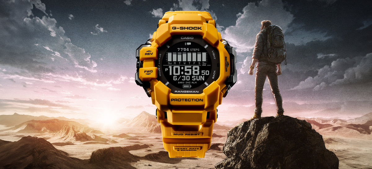 Bright yellow G-SHOCK Rangeman digital watch featuring a rugged mud-resistant design against a desert mountain landscape.