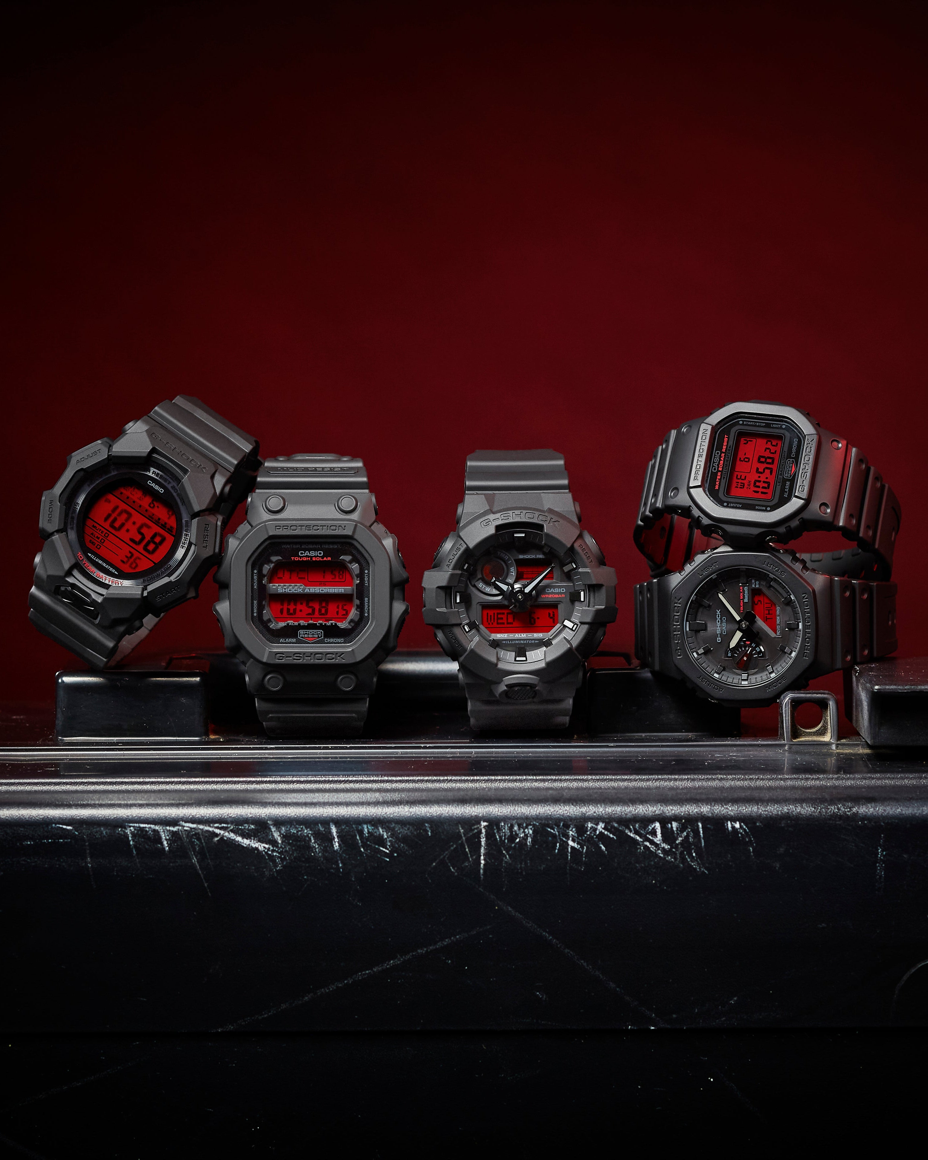 Five black resin watches with red accents on a dark background
