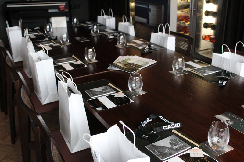 Dark wooden conference table set with white gift bags, glasses, and event brochures for a Casio and Rydges hotel meeting.
