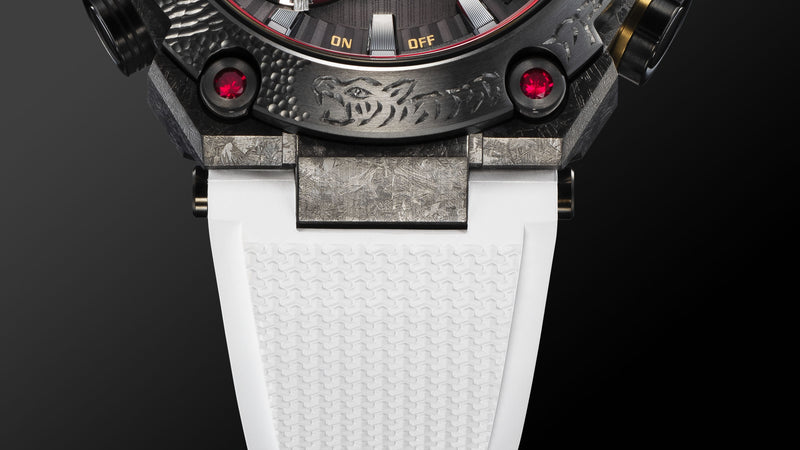 Close-up of a G-SHOCK MR-G watch featuring a tiger engraving, red ruby accents, and a textured white rubber strap.