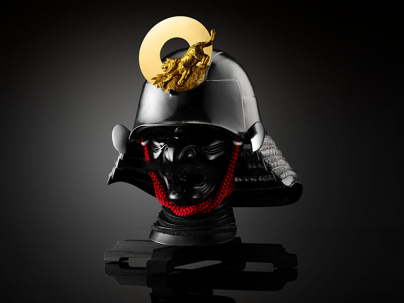 Black samurai helmet with a gold tiger crest, red cord accents, and a fierce black mask on a dark reflective surface.