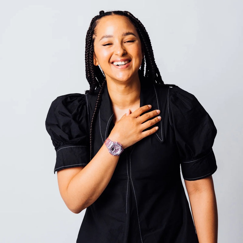 Smiling woman with braided hair wearing a black puff-sleeve dress and a translucent pink wristwatch.