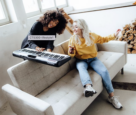 Two women laughing on a beige sofa while one plays a portable Casio keyboard.