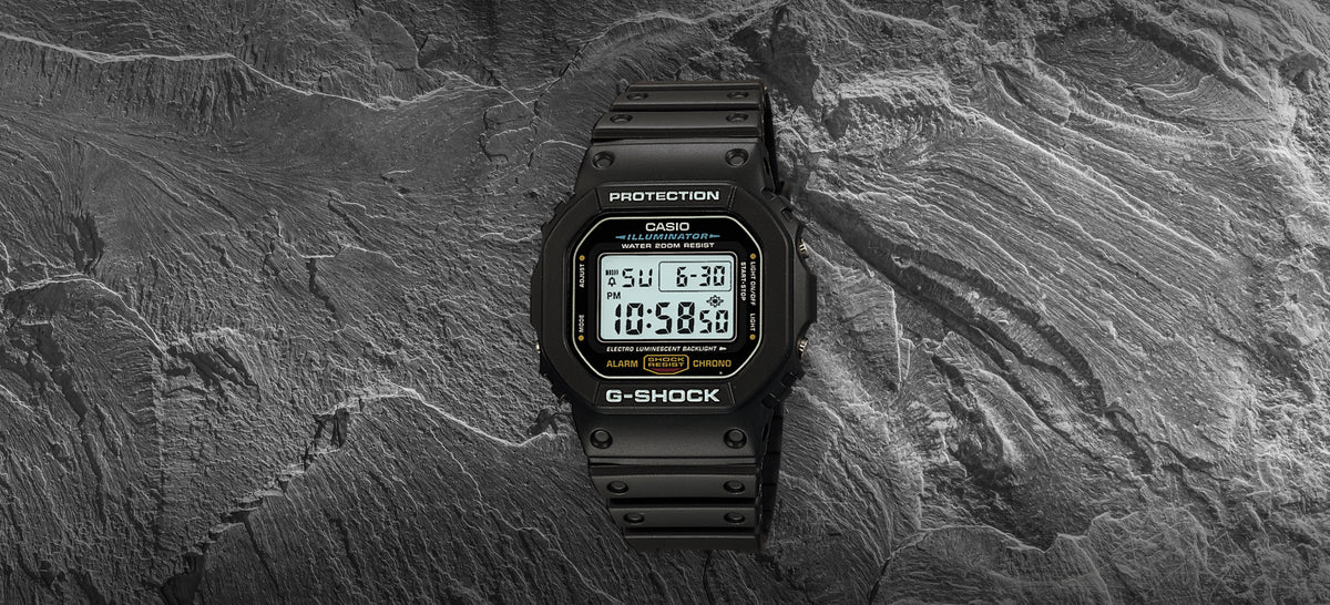 Black Casio G-Shock digital watch with a square face resting on a textured dark grey stone background.
