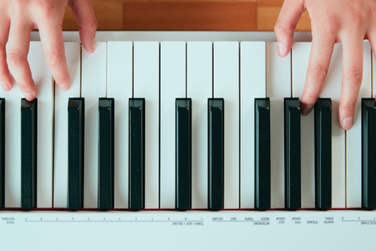 Hands playing a white Casio digital keyboard with black keys, viewed from a top-down perspective.