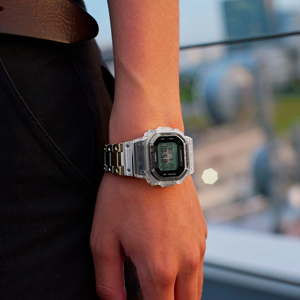 Person wearing a G-Shock watch with a transparent resin case and a metallic silver link bracelet.