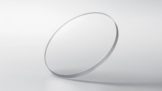A single, clear circular optical lens floating against a minimalist, soft-focus white background.