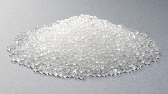 A pile of small, translucent plastic resin pellets resting on a smooth, grey surface.