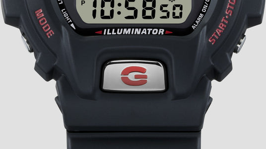 Close-up of a black digital watch with a chrome G-logo button, Illuminator display, and red text accents.