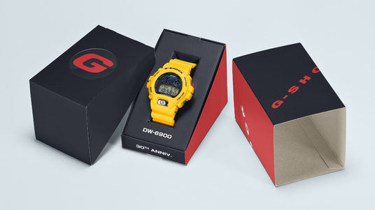 Bright yellow Casio G-Shock DW-6900 30th anniversary watch displayed in its branded black and red presentation box.
