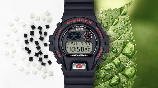 Black Casio G-Shock digital watch between white plastic pellets and a dew-covered green leaf.