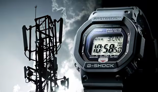 Black Casio G-Shock digital watch displayed next to a silhouetted telecommunications tower against a cloudy sky.