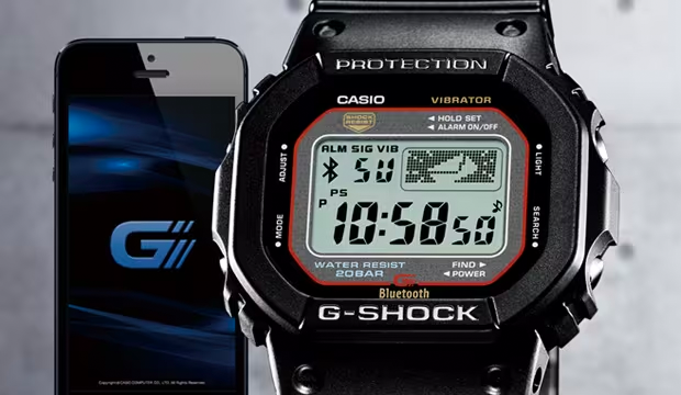 Black Casio G-Shock digital watch with Bluetooth connectivity next to a smartphone displaying the G-Shock app logo.